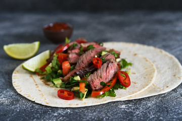 Classic Mexican dish - corn tortilla with vegetables and beef on a kitchen stone table.