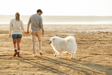 Couple outdoors at beach walking with dog samoyed.