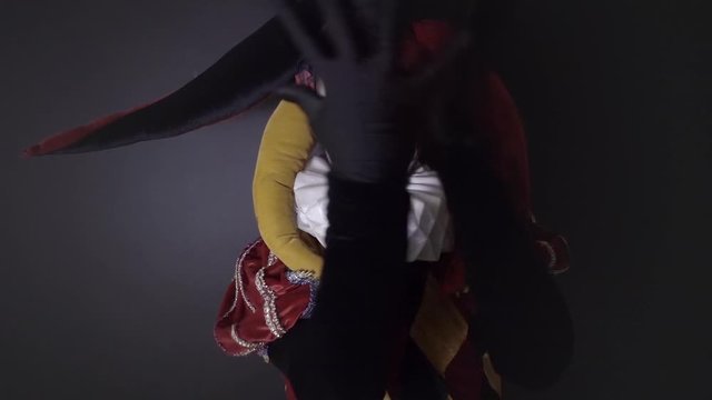Street artist in an old costume of Jester, circus performance happy harlequin. Slow motion	