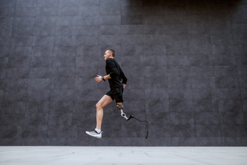 Side view of handsome fit caucasian sportsman with artificial leg running outside.