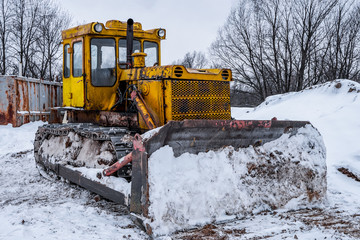 Yellow excavator on new construction site, with the bright sun and nice blue sky in the background. Yellow bulldozer in the winter on the street, snowdrifts and snow slopes
