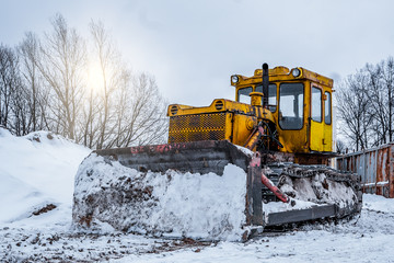 Yellow excavator on new construction site, with the bright sun and nice blue sky in the background. Yellow bulldozer in the winter on the street, snowdrifts and snow slopes © Алексей Закиров