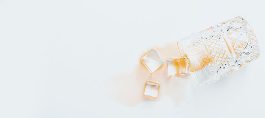 overturned glass with whiskey on a white background, ice cubes fell out of a glass