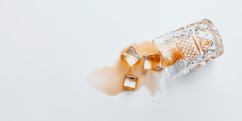 overturned glass with whiskey on a white background, ice cubes fell out of a glass
