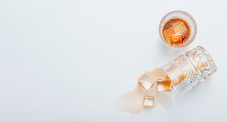 a glass of whiskey next to an overturned glass of whiskey on a white background, ice cubes fell out of a glass
