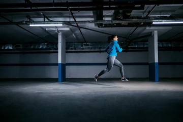 Young fit attractive caucasian sportswoman in tracksuit running fast in garage. Urban life concept.