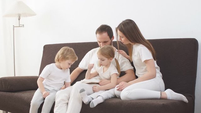 Portrait of a young full-fledged family in light clothes, spend fun together on the couch.