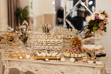 Table full with cakes and sweets at a wedding reception. Wedding candy bar and different cap cakes. Candy bar, a table with sweets and desserts on the table. Buffet with delicious cupcakes, flowers.