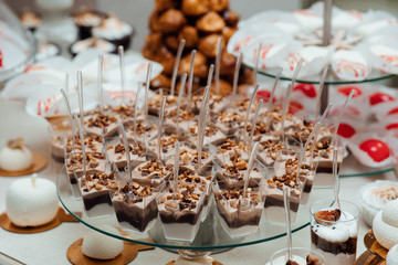 Candy bar. White wedding cake decorated by flowers standing of festive table with deserts, strawberry tartlet and cupcakes. Wedding. Reception Tartlets. Bithday cakes and accesories. 