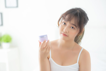 Beautiful portrait young asian woman holding and presenting cream or lotion product, beauty asia girl show cosmetic makeup and moisturizing for skin care, healthy care and wellness concept.