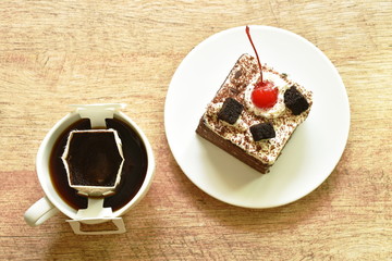black fotest cake with cream topping cherry and hot coffee drip filter in cup