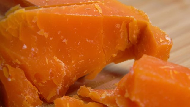 Knife cuts and breaks a hard french orange-colored Mimolette cheese on a wooden board