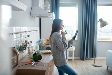 Dark-haired girl in a grey sweater reading news in the morning