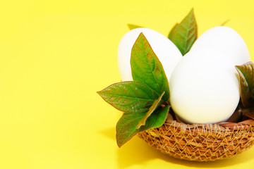 white eggs and green leaves in a decorative straw plate for Easter