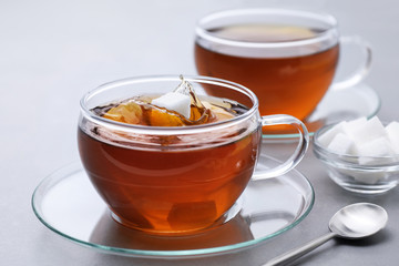 Sugar cube falls in a cup of tea on a gray background.