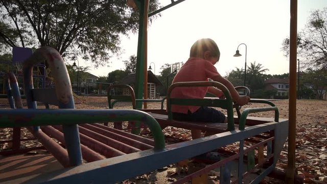 Slow Motion backlit video of a happy little asian boy in the playground pretending and imagining he is driving a bus with the sun behind him