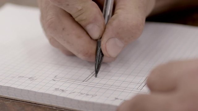 A craftsman draws plans for a construction in a notebook with a mechanical pencil, close up