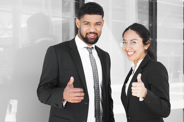 Happy confident business partners enjoying teamwork. Smiling young man and woman in office suits showing thumb up gestures. Best team concept