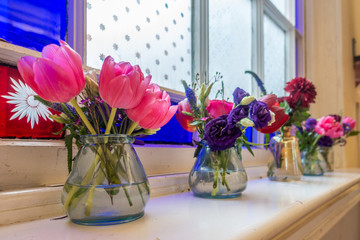 Cut flowers in glass vases on a window sill in front of a stained glass window