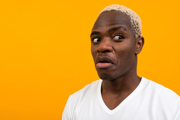 charismatic african man in a white t-shirt with a mock looks surprised to the side on a yellow studio background with copy space