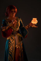 Beautiful redhead woman in cosplay costume with magic lamp on grey background