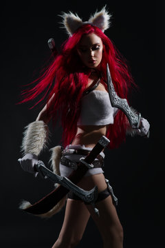Sexy redhead woman in cosplay costume of warrior cat with swords posing on dark background