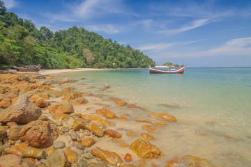 view of many rocks on sand beach with a fishing boat floating in blue-green sea and blue sky background, Kwang Peeb beach (Ao Kwang Peeb), Ko Phayam (ko payam), Ranong, Thailand.