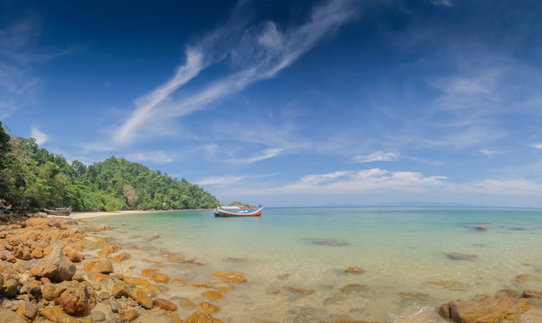 view of many rocks on sand beach with a fishing boat floating in blue-green sea and blue sky background, Kwang Peeb beach (Ao Kwang Peeb), Ko Phayam (ko payam), Ranong, Thailand.