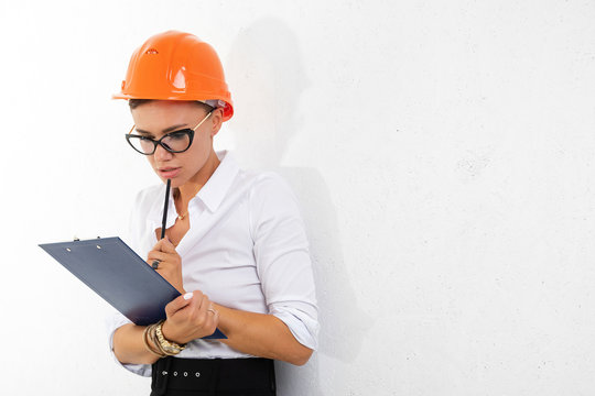 Cheerful lady with short dark hair, in beautiful office suit, orange comstruction helmet plans something with tablet isolated on white background
