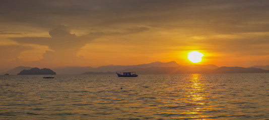 Fototapeta na wymiar Sea view morning of a fishing boat running in the sea with yellow sun light in the sky background, sunrise at front beach, Ko Phayam island, Ranong, southern of Thailand.