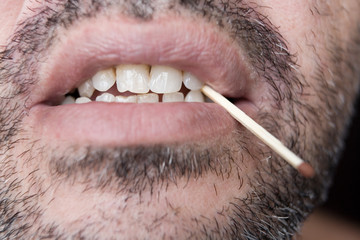 A match in the teeth of an unshaven man.