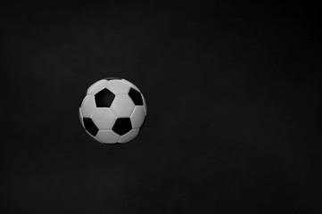 Fototapeta na wymiar A black-and-white soccer ball flies in the air, isolated on a dark background. The concept of object levitation. Minimalistic black color. Levitating objects. Macro mode.