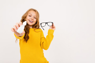 Happy teenager girl with red hair, hoody and yellow trousers holds contact lenses and glasses...