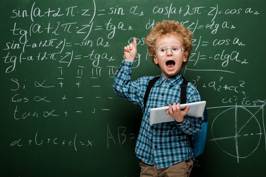 smart kid in glasses having idea while holding digital tablet near chalkboard - Powered by Adobe