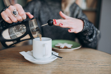 Fototapeta na wymiar a girl in a sweater pours coffee into a white Cup from a French press