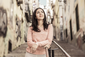 Relaxed young woman leaning on city stairs railing. Pretty lady standing with graffiti walls in background. Urban lifestyle concept. Front view.