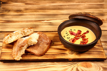 Thick cream soup with herbs and seasonings in a clay pot with bread. Proper balanced nutrition. Vegetarian vegetable soup. Dish menu on a wooden board. Fragrant hot food. High-calorie food.