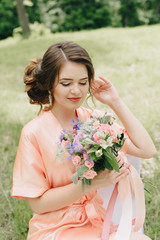 beautiful girl in a bathrobe with a bouquet of flowers on nature in summer on a background of green leaves