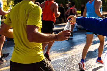 A helping hand delivers a bottle of water to a runner in a running race for him to drink.