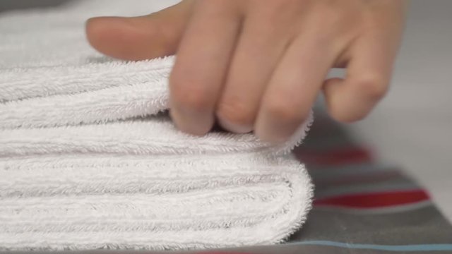 Close-up of hands putting stack of fresh white bath towels on the bed sheet. Room service maid cleaning hotel room macro closeup