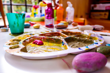 Children choosing colors in a paint palette with a brush enjoying art at home.