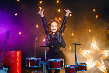 Beautiful girl with curly hair playing the drums on a black illuminated background