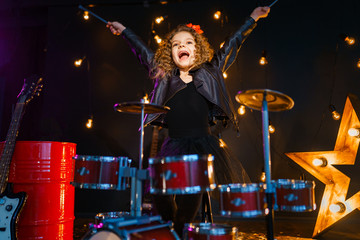 Beautiful girl with curly hair playing the drums on a black illuminated background