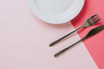 Empty white plate with cutlery on a pink-peach background. Top view