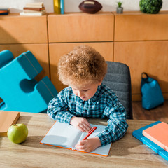 cute smart kid writing in notebook near books and apple