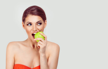 Obraz na płótnie Canvas One apple a day keep doctor away. Cute woman eating an apple fruit looking to the side in a studio isolated white background wall