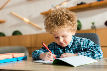 smart child writing in notebook near books on table