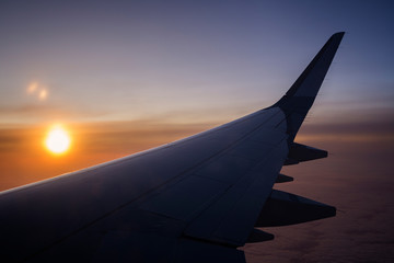 Flying above the clouds. Scenic view of sun, cloudy sky and airplane wing at sunset.