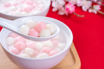Fototapeta na wymiar Tang yuan, tangyuan, delicious red and white rice dumpling balls in a small bowl on red background. Asian festive food for Chinese Winter Solstice Festival, close up.