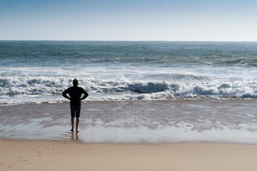 A man walking along blue ocean